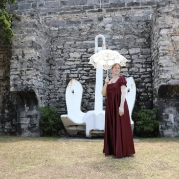 A woman in a red dress poses gracefully in front of a textured stone wall, showcasing elegance and style.