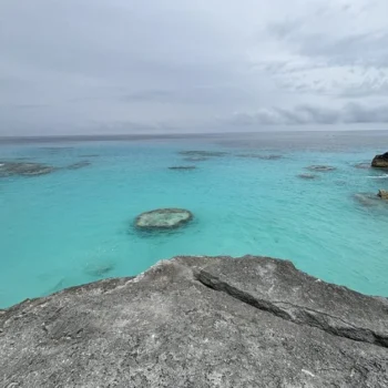 A breathtaking view of the ocean in Bermuda stretching out from a rugged rocky cliff under a clear blue sky.